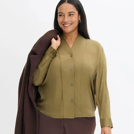 Elegantní kombinace olivově zelené blůzy a hnědého kabátu.