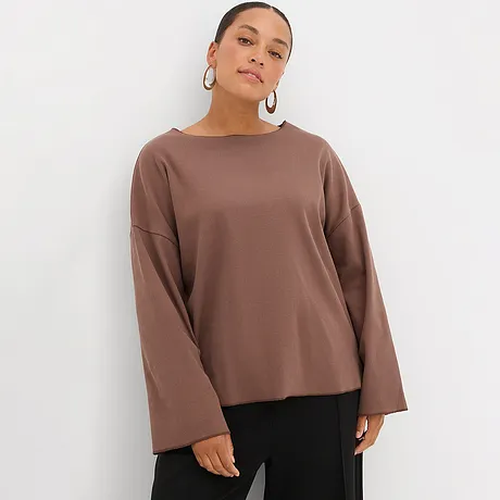 Hnědé tričko s dlouhým rukávem a širokými rukávy v kombinaci s černými kalhotami.