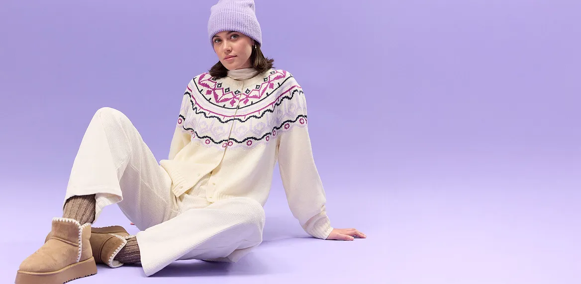 Krémový svetr se severským vzorem, bílé kalhoty a fialová pletená čepice.