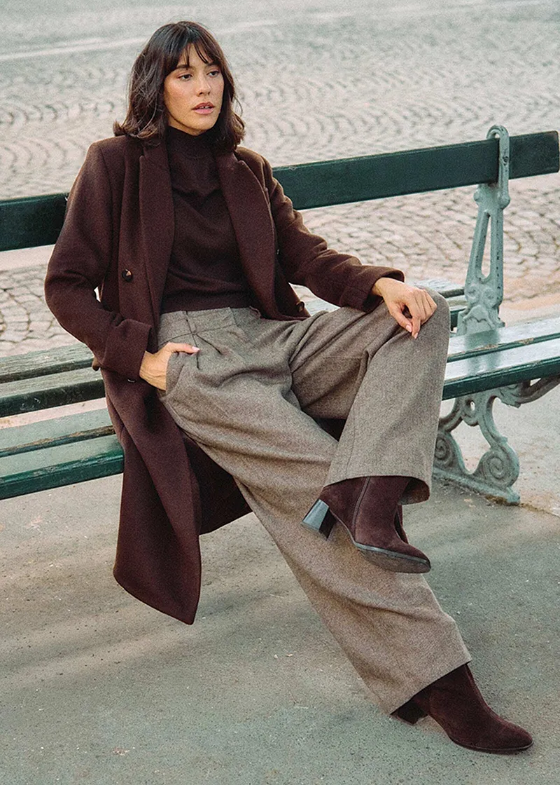 Dlouhý hnědý kabát, rolák a široké tvídové kalhoty.