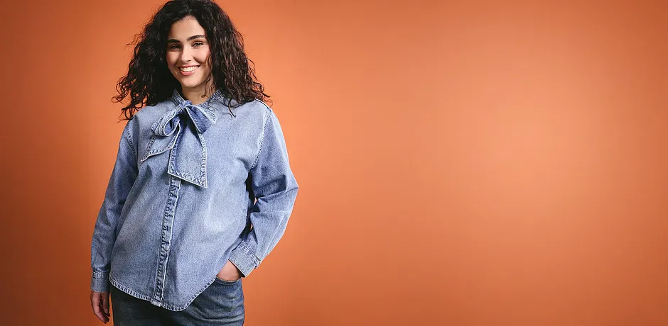 Světle modrá džínová košile s mašlí na límci dodává outfitu ležérní šarm.