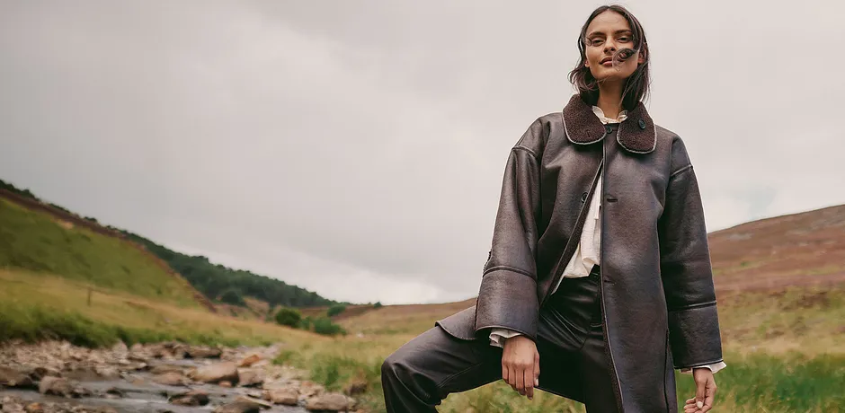 Elegantní hnědý kožený kabát s velkým límcem v kombinaci se světlým topem a tmavými kalhotami.