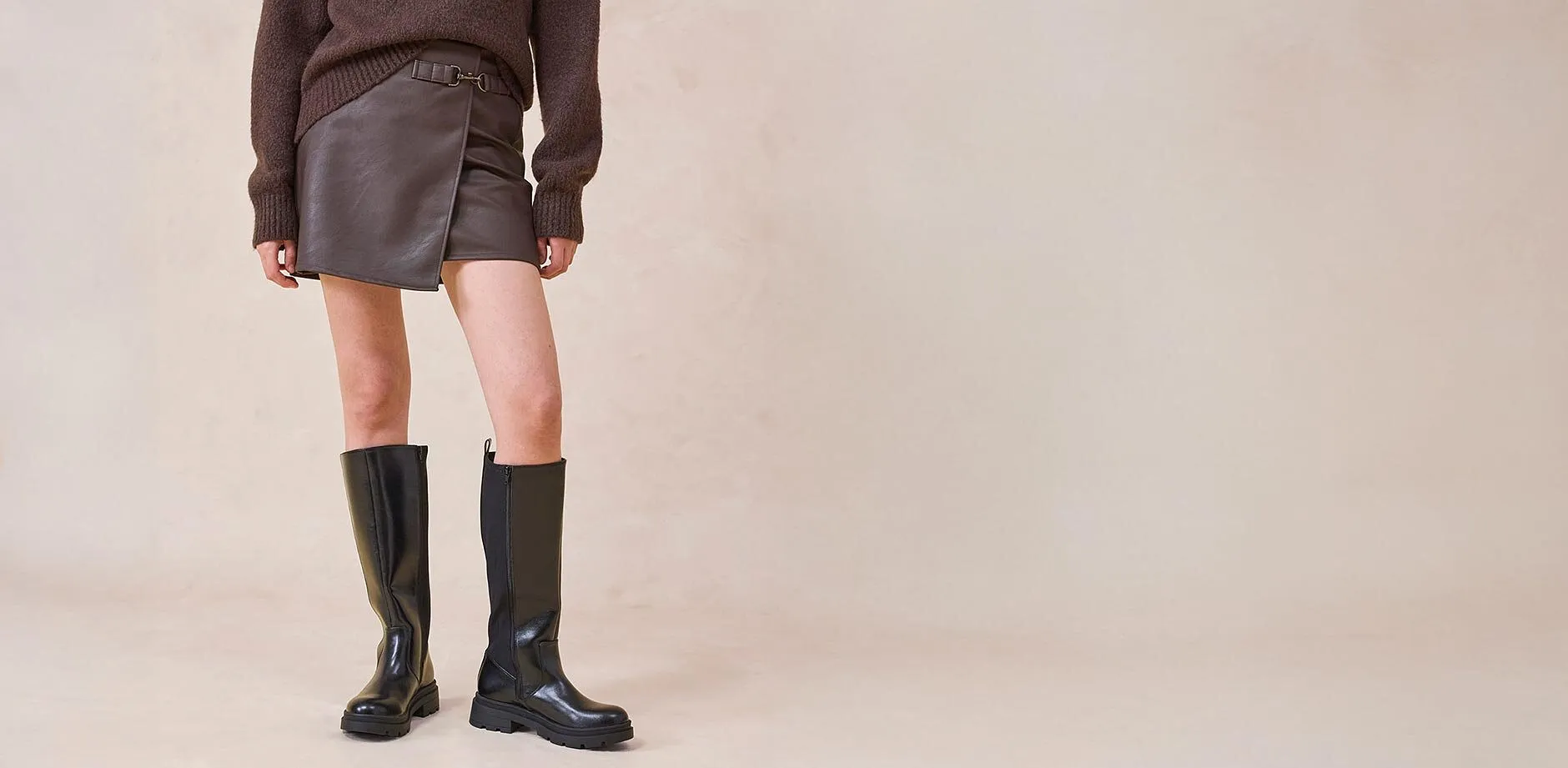 Kožená sukně a kolenní boty v kombinaci s hnědým svetrem.