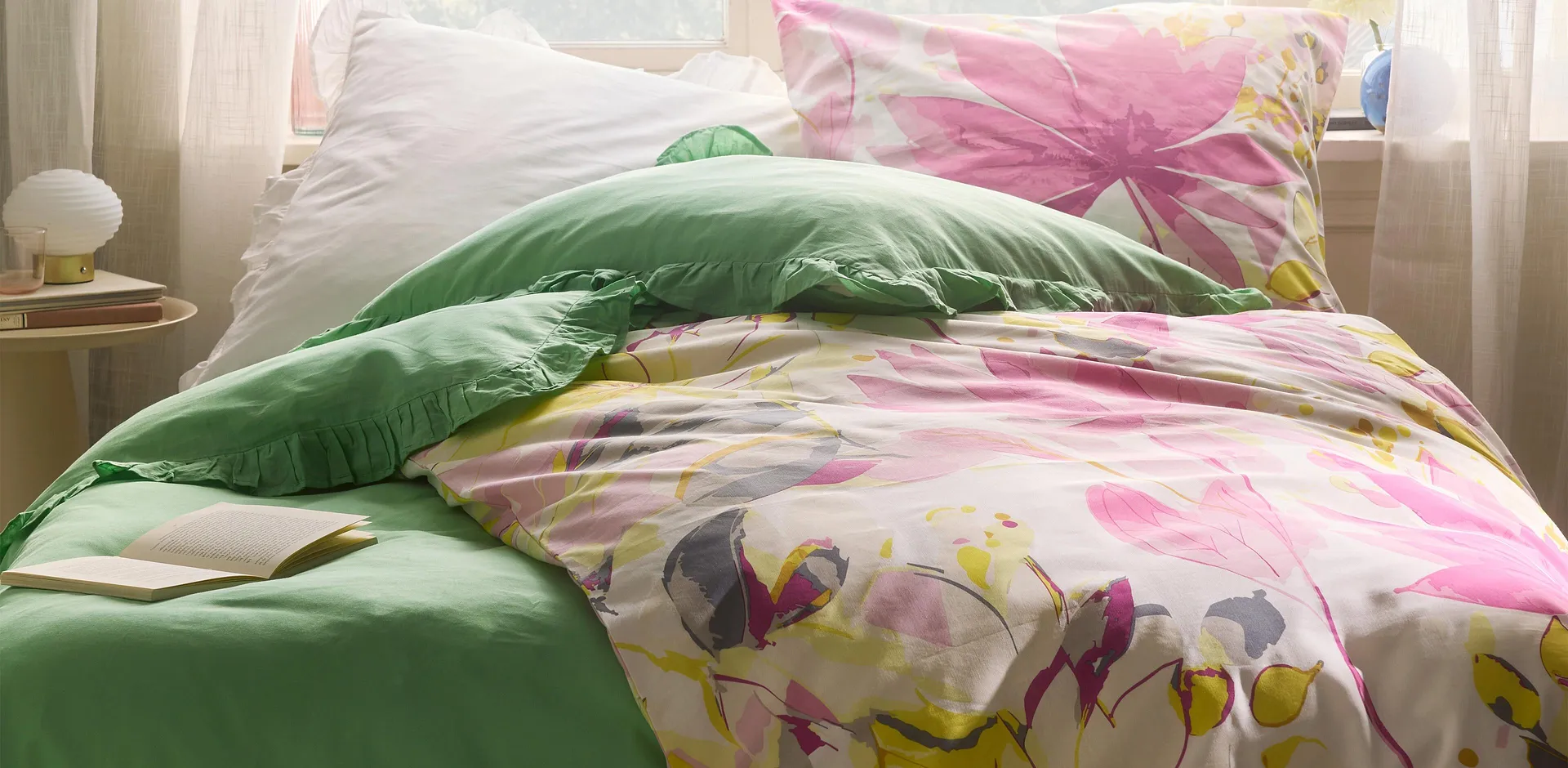 Barevn&eacute; povlečen&iacute; s květinov&yacute;m vzorem v kombinaci se zelen&yacute;m pol&scaron;t&aacute;řem. Postel r&aacute;muj&iacute; jemn&eacute; z&aacute;clony.