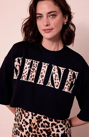 Žena v tričku SHINE Leo a sukni Leo před světlou stěnou