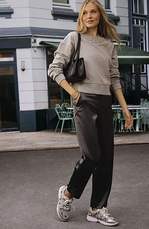 Ležérní streetstyle: béžový svetr, tmavé kalhoty a bílé tenisky. Černá kabelka jako doplněk.