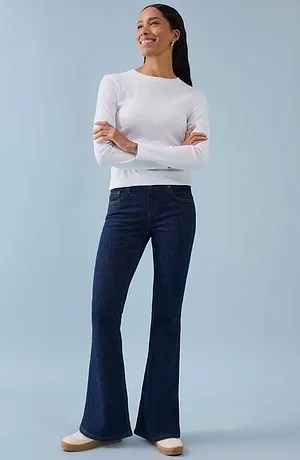 Bílé tričko s dlouhým rukávem v kombinaci s tmavě modrými zvonovými kalhotami pro nadčasový, elegantní vzhled.