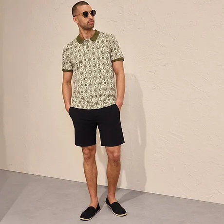 Gemustertes Poloshirt und dunkle Shorts bilden einen lässigen Sommerlook, ergänzt durch Sonnenbrille und Espadrilles.