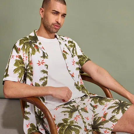 Tropisches Hemd und Shorts mit Palmen-Muster, darunter ein schlichtes weißes T-Shirt.