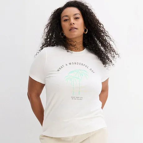 Weißes T-Shirt mit grünem Palmen-Aufdruck und Schriftzug, lässig kombiniert mit heller Hose.