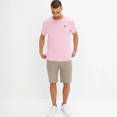 Růžové tričko s malým logem a béžové šortky tvoří letní outfit.