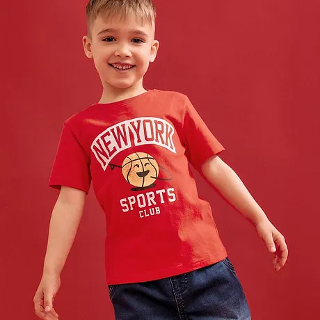 Červené tričko s nápisem „New York Sports Club“ v kombinaci s modrými džínami.