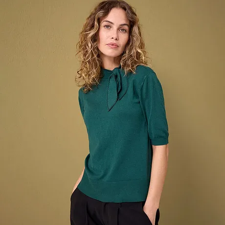 Elegantní smaragdově zelený svetr s krátkými rukávy v kombinaci s tmavými kalhotami.