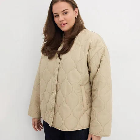 Béžová prošívaná bunda s knoflíky v kombinaci s tmavými kalhotami.