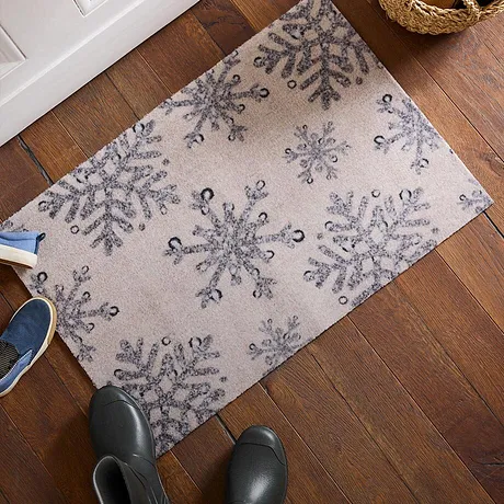 Zimní rohožka se vzorem sněhových vloček na dřevěné podlaze.