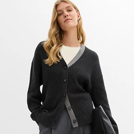 Tmavý pletený kardigan přes bílou košili, kombinovaný se šedou sukní a černou taškou.