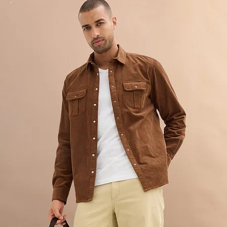 Hnědá košile přes bílé tričko, kombinovaná se světlými kalhotami.