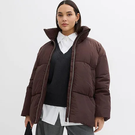 Hnědá zimní bunda s vysokým límcem, pod ní tmavý svetr a bílá košile.