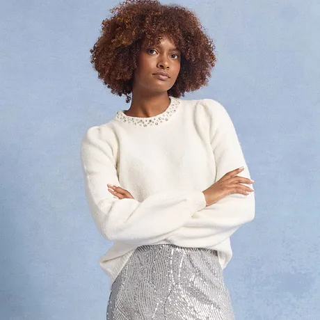 Bílý svetr s krajkovým límcem v kombinaci s třpytivou stříbrnou sukní.