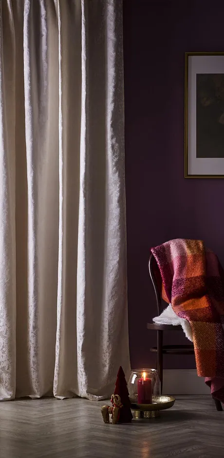 Světlé záclony zdobí okno. Na židli leží teplá deka.