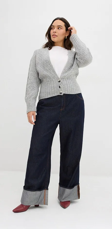 Šedý pletený svetr přes bílé tričko, tmavé džíny s ohrnutými nohavicemi a červené boty.