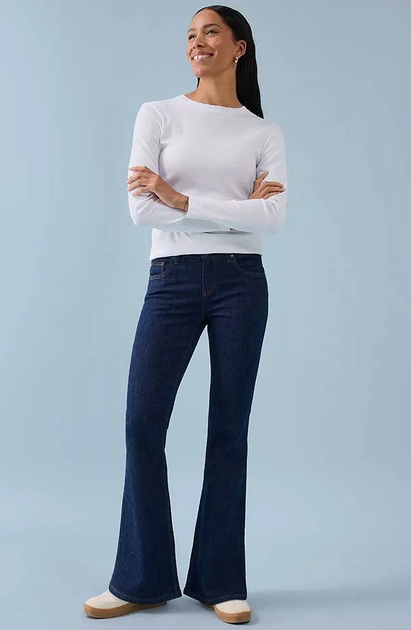 Bílé tričko s dlouhým rukávem v kombinaci s tmavě modrými zvonovými kalhotami pro nadčasový, elegantní vzhled.