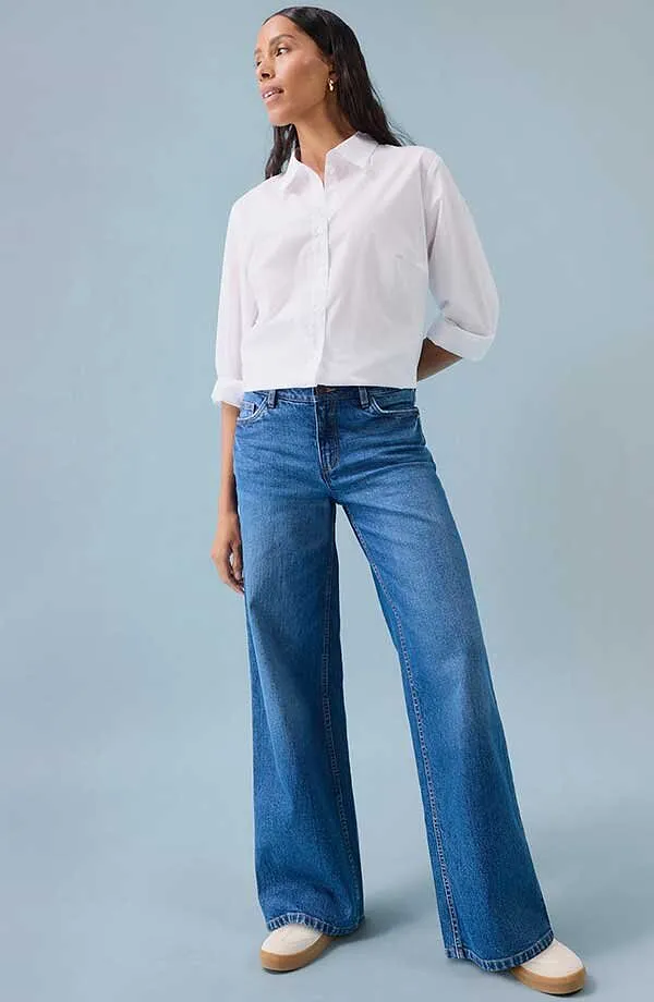 Bílá košile k modrým džínám s širokými nohavicemi a bílými botami.