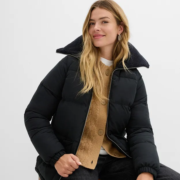 Čern&aacute; zimn&iacute; bunda s vysok&yacute;m l&iacute;mcem přes žlut&yacute; pleten&yacute; svetr a b&iacute;lou ko&scaron;ili.