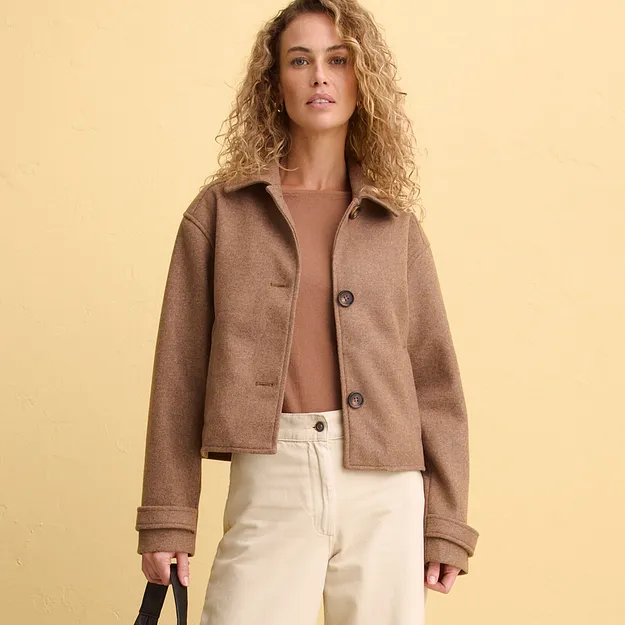 Elegantn&iacute; hněd&aacute; kr&aacute;tk&aacute; bunda přes jemn&yacute; top, kombinovan&aacute; se světl&yacute;mi kalhotami.