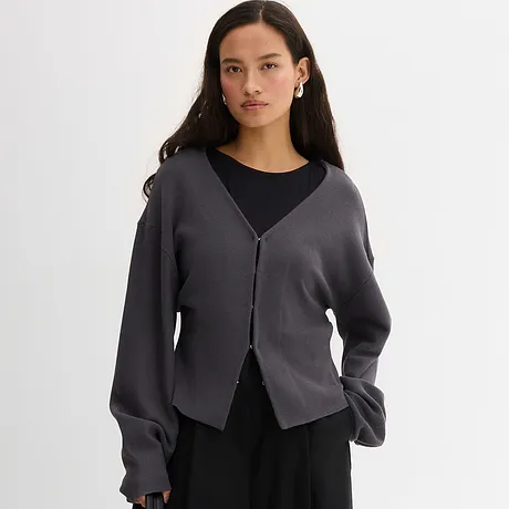 Elegantní šedý kabátek přes černý top. Ležérní vzhled s výstřihem do V a knoflíkovou légou.