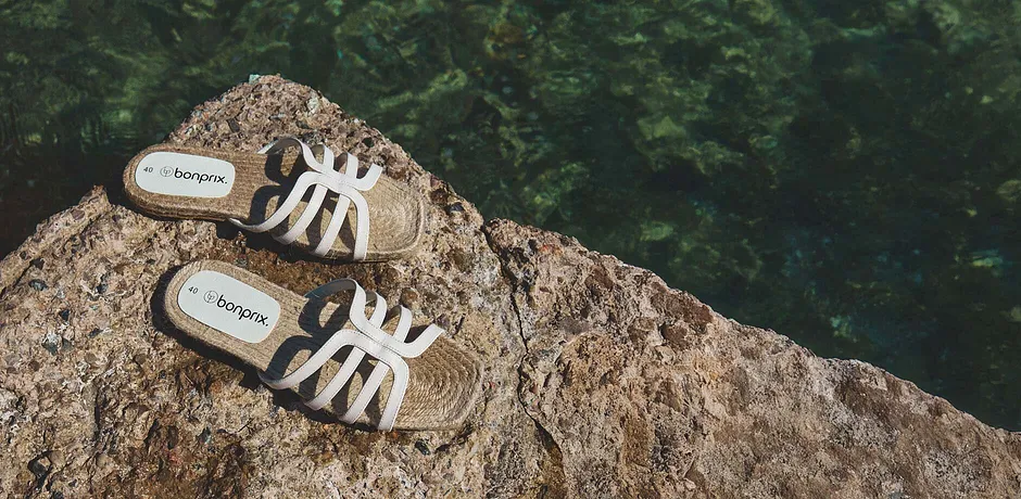 Weiße Sandalen auf felsigem Untergrund am Strand.