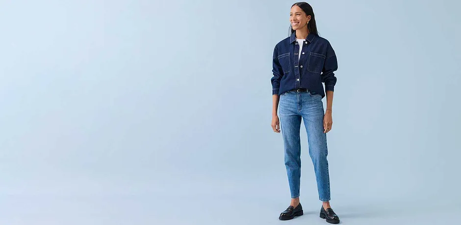 Ležérní look s džínovou bundou, bílou košilí a světle modrými džínami. Outfit doplňují tmavé boty.