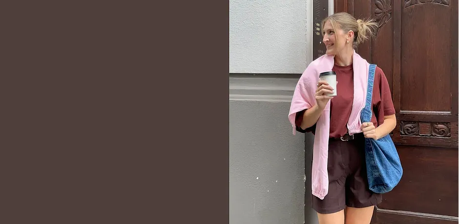 Letní outfit s růžovým svetrem, hnědými šortkami a modrou taškou.