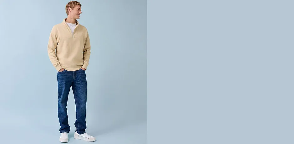 Béžový svetr se zipem, modré džíny a bílé tenisky – ležérní každodenní look pro muže.