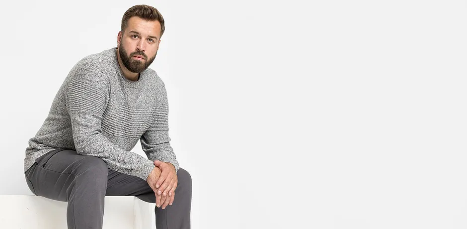 Šedý pletený svetr a šedé kalhoty tvoří ležérní outfit.