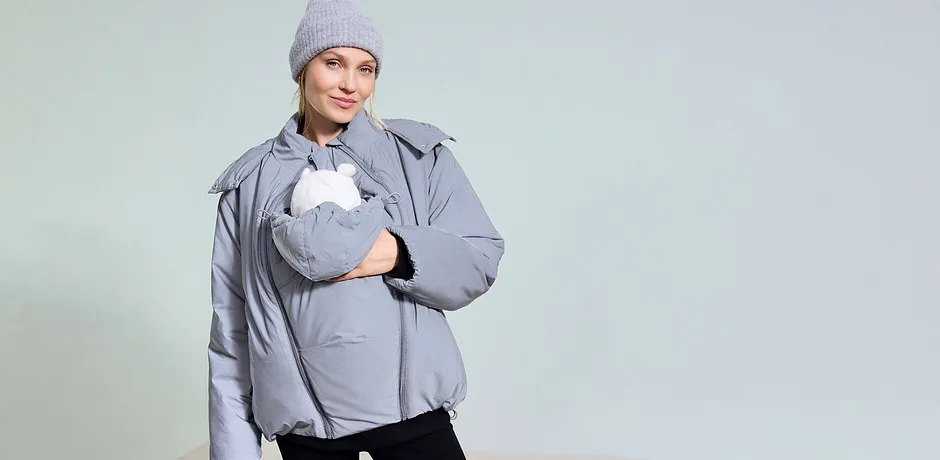 Šedá těhotenská a nosicí bunda v kombinaci se šedou čepicí.