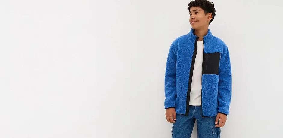 Modrý fleecový svetr s černým vsadkou, kombinovaný s džíny a bílým tričkem.