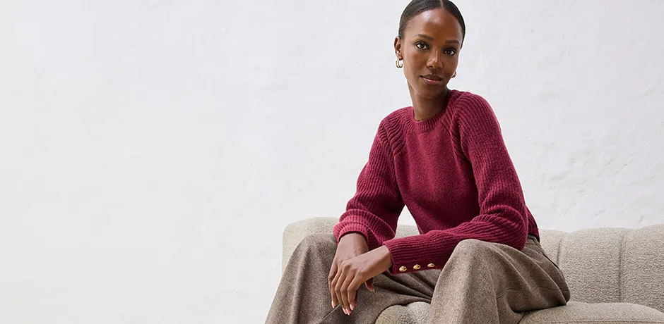 Červený svetr s béžovými kalhotami na světlé pohovce.