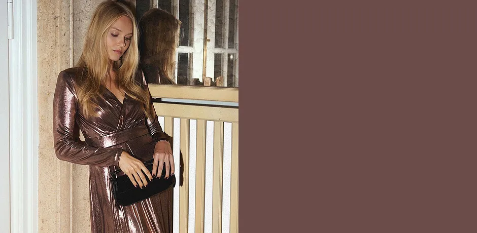 Třpytivé šaty s výstřihem do V v kombinaci s černou kabelkou.