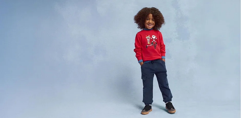 Červený svetr s vánočním motivem, modré džíny a hnědé boty.