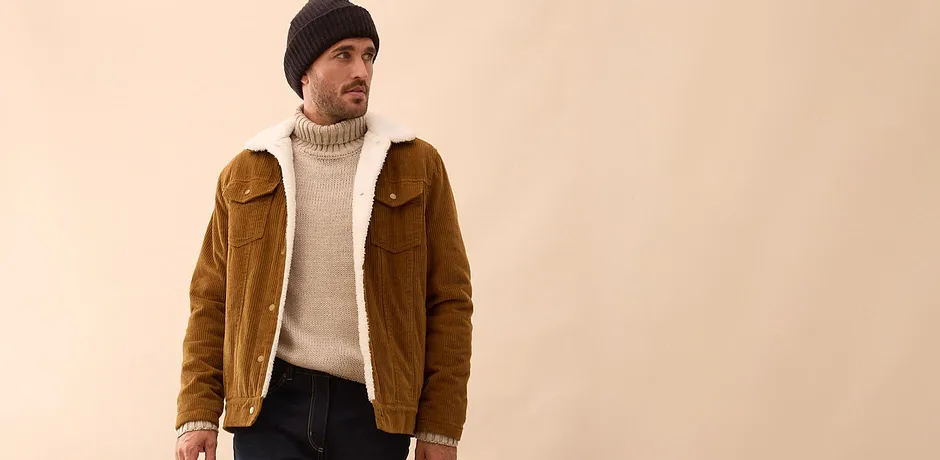 Hnědá manšestrová bunda přes krémový rolák, k tomu tmavé džíny a čepice.