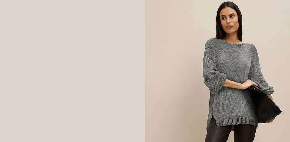 Šedý dlouhý svetr v kombinaci s tmavými kalhotami.