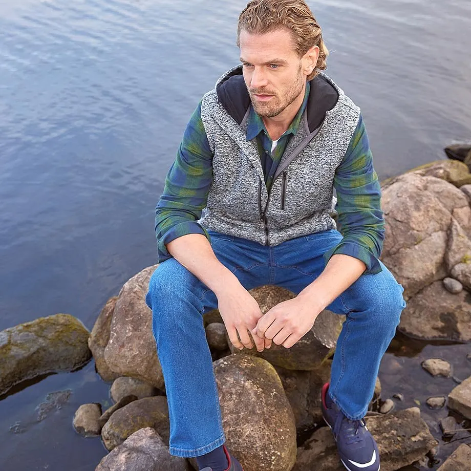 Vzorovaná vesta přes zelenou košili, kombinovaná s modrými džíny.