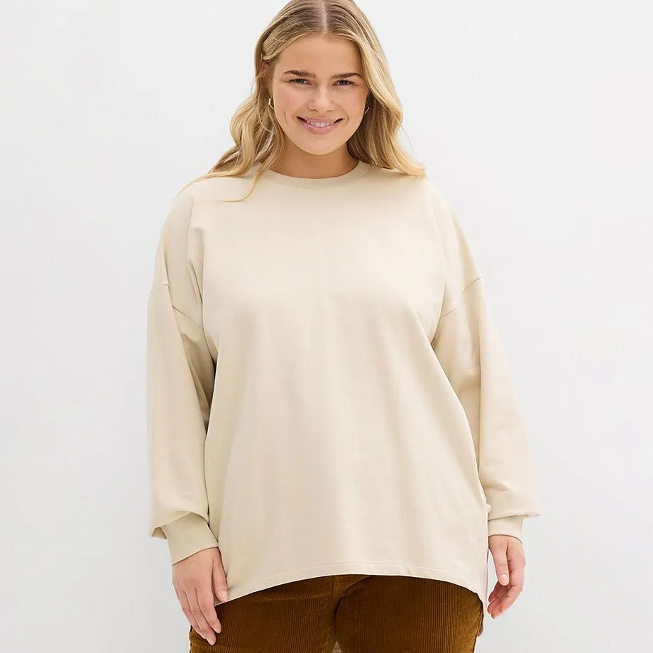 Krémová mikina s kulatým výstřihem v kombinaci s hnědými kalhotami.