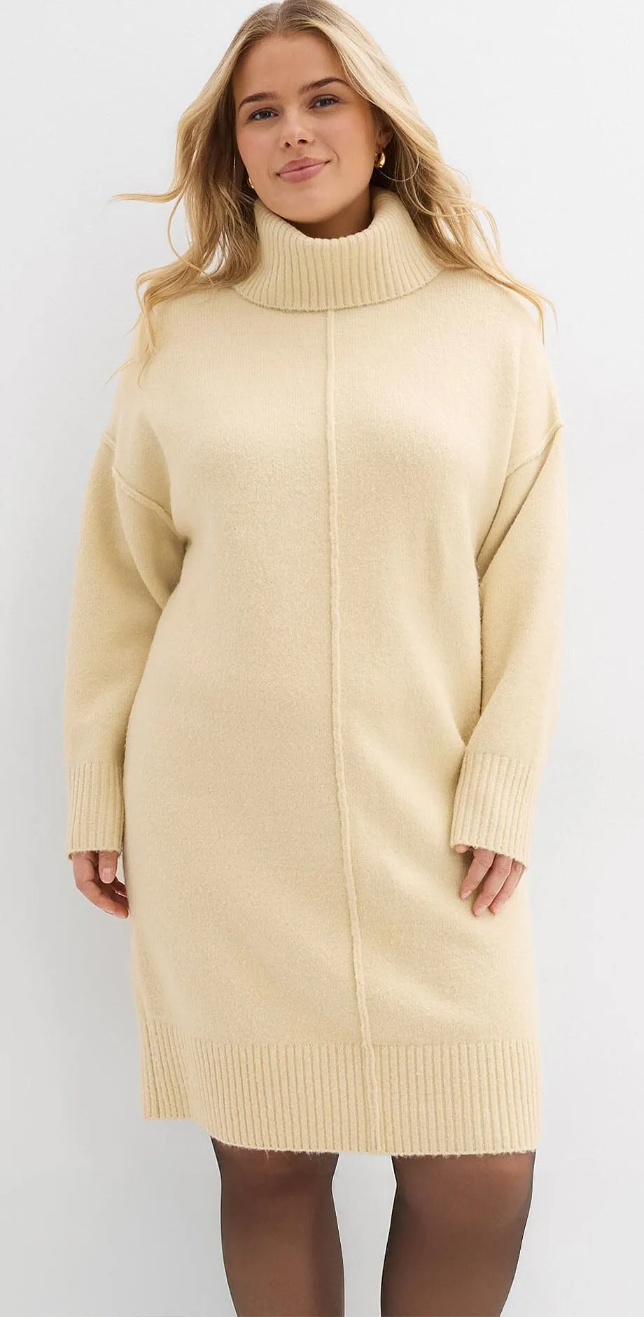 Krémově bílé pletené šaty s vysokým límcem a dlouhými rukávy.