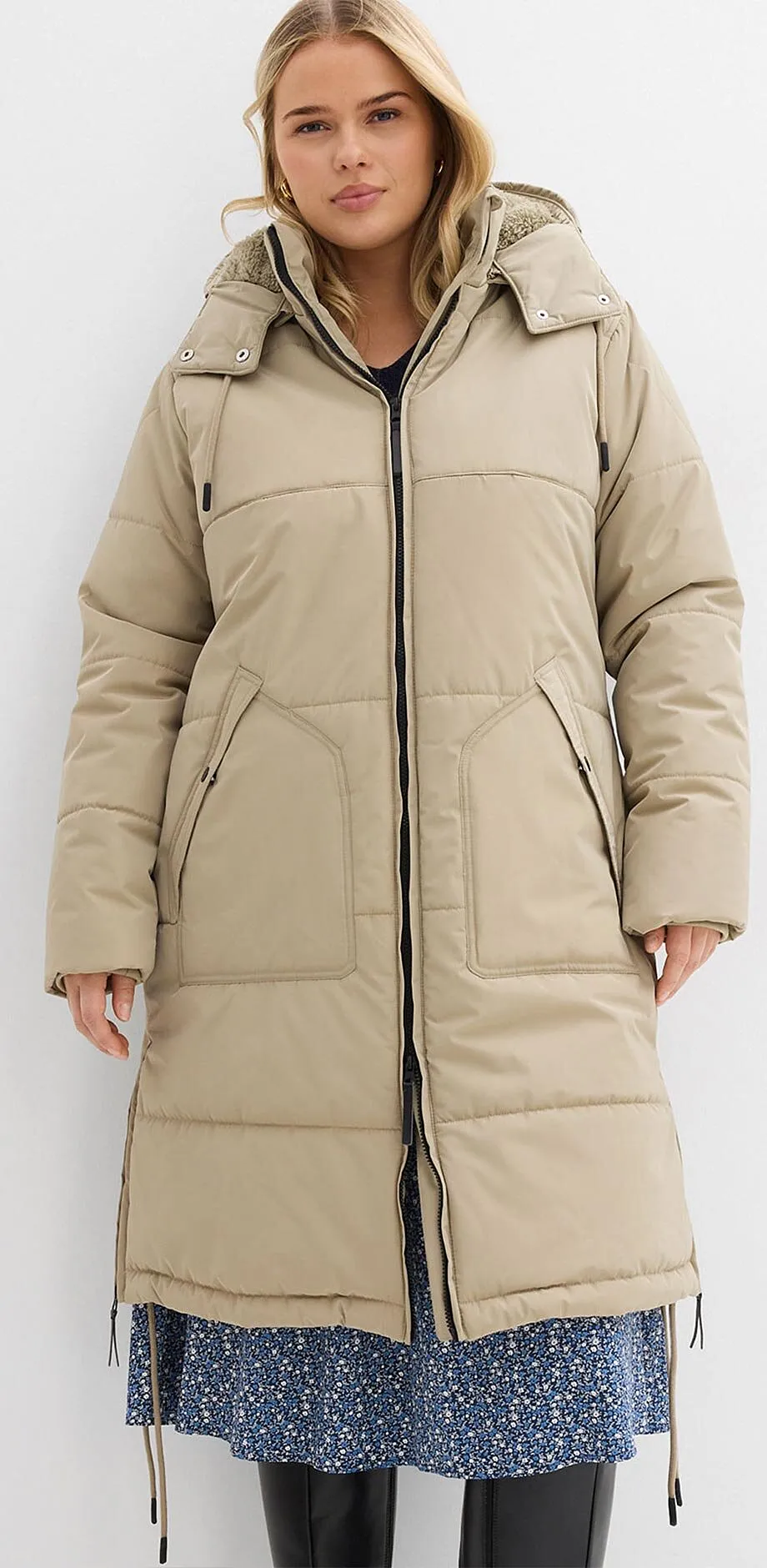 Béžový prošívaný kabát s kapucí přes modré květinové šaty. 