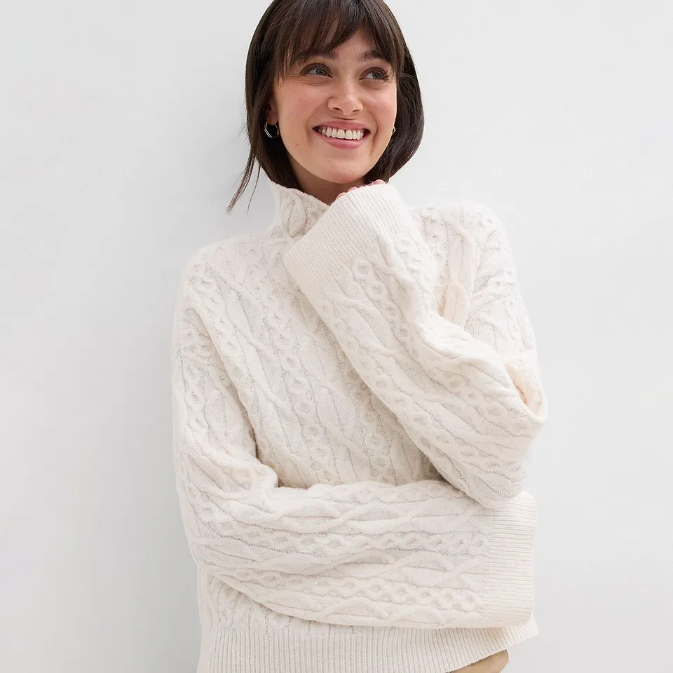 B&iacute;l&yacute; pleten&yacute; svetr s vysok&yacute;m l&iacute;mcem a strukturovan&yacute;m vzorem.