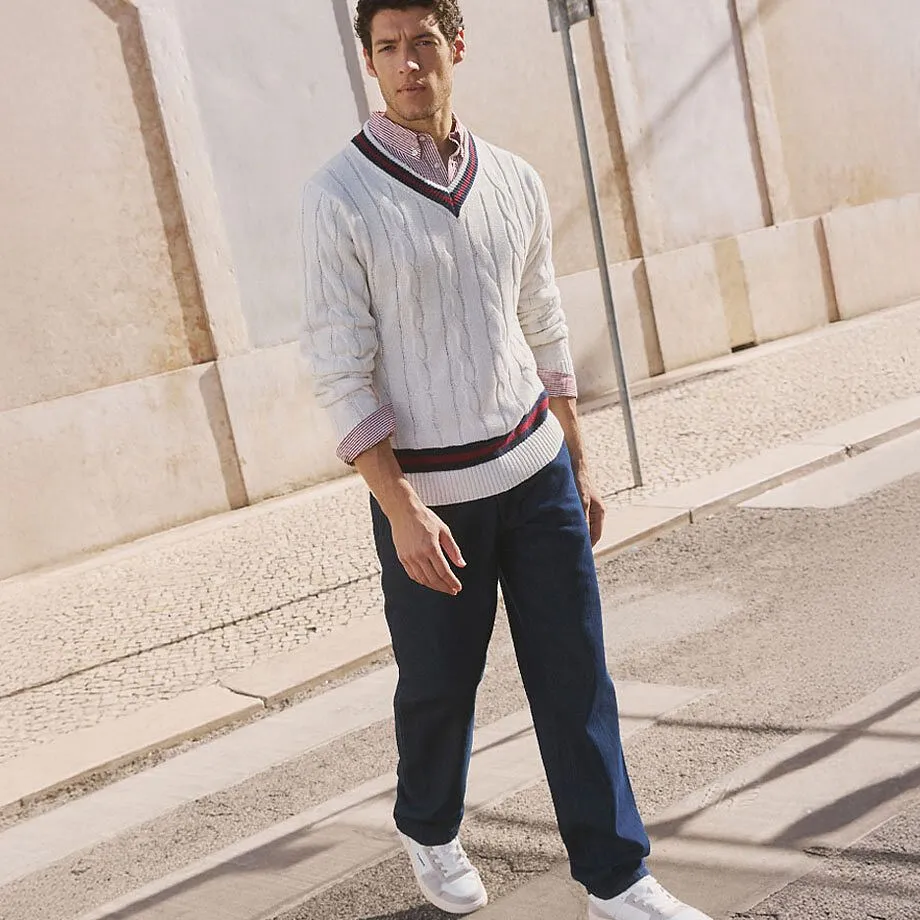 B&iacute;l&yacute; svetr s cop&aacute;nkov&yacute;m vzorem přes ko&scaron;ili, tmav&eacute; kalhoty a b&iacute;l&eacute; tenisky.