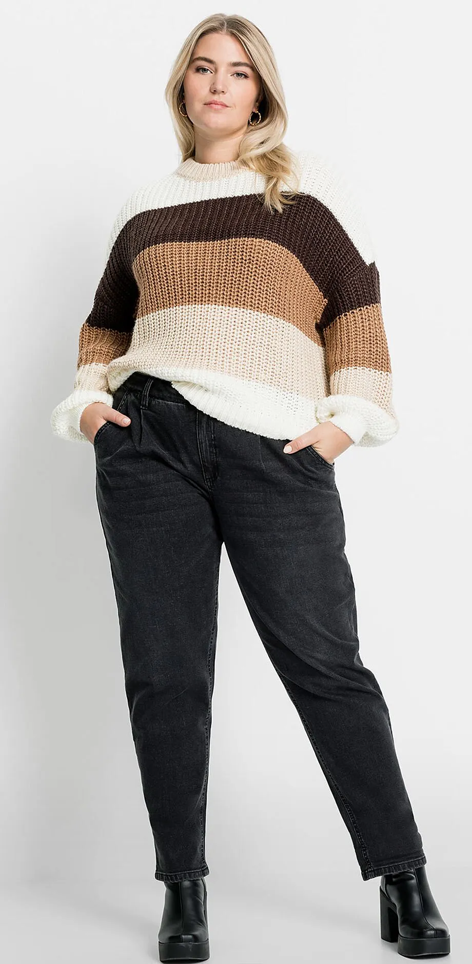 Pruhovan&yacute; pleten&yacute; svetr v zemit&yacute;ch t&oacute;nech v kombinaci s tmav&yacute;mi dž&iacute;ny a čern&yacute;mi botami.