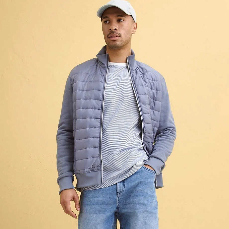 &Scaron;edo-modr&aacute; pro&scaron;&iacute;van&aacute; bunda přes světle &scaron;ed&eacute; tričko, modr&eacute; dž&iacute;ny.